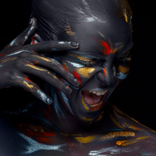 Portrait of a young woman who is posing covered with  black paint