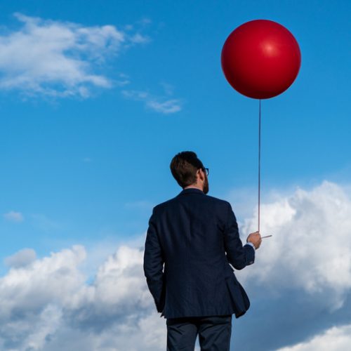 Businessman Holding Red Balloon Against Blue Cloudy Sky
